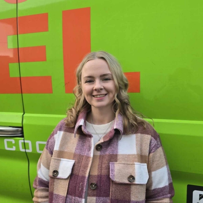 ServiceXEL team member wearing checkered jacket smiling in front of company-branded green and orange van