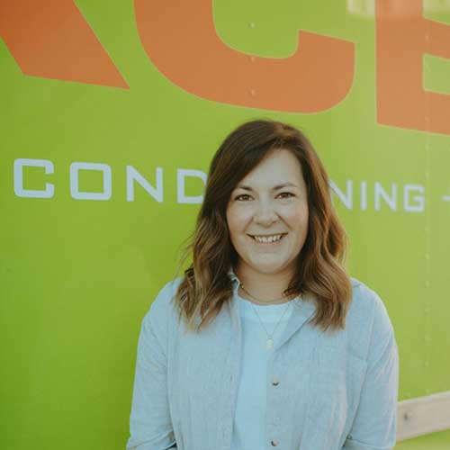 ServiceXEL team member smiling in light blue shirt in front of green and orange branded service vehicle