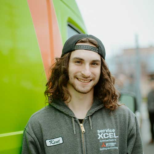 ServiceXEL technician wearing hoodie and cap, smiling in front of a green company van