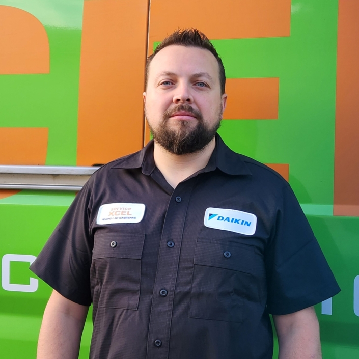 ServiceXEL technician in uniform standing in front of green and orange service van