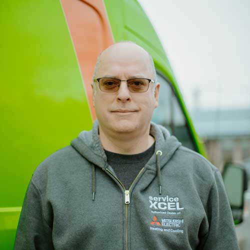 ServiceXEL technician in branded hoodie with Mitsubishi Electric logo, standing in front of green and orange van