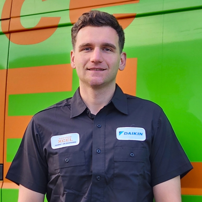 ServiceXEL technician in uniform standing in front of a green and orange company-branded service van