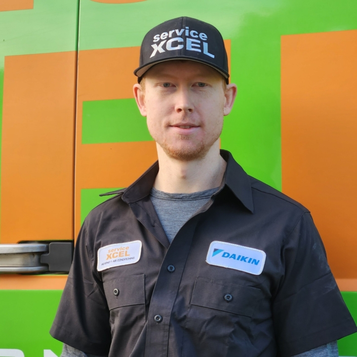 ServiceXEL technician in branded uniform and cap standing in front of company vehicle